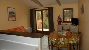 Un comedor con una mesa dispuesta para dos personas, un sofá, un televisor y un balcón con vistas.