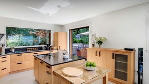 Eine moderne Küche mit einem großen Fenster, Holzschränken, einem Glastisch und einer Schüssel grüner Äpfel.