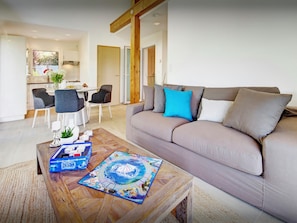Una sala moderna con un sofá color beige, una mesa de centro de madera, y un comedor con una mesa blanca y sillas grises.