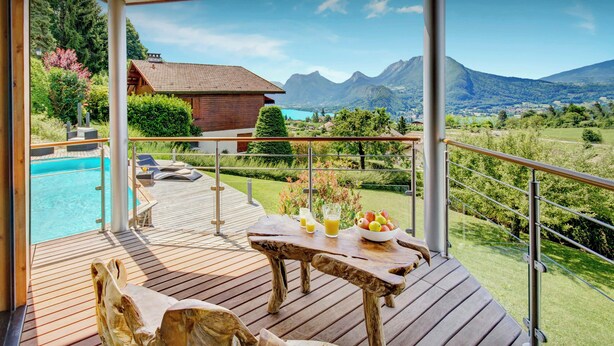 Eine Holzterrasse mit Tisch und Stühlen mit Blick auf einen Swimmingpool und eine gebirgige Landschaft.