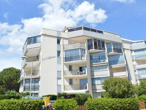 Un hôtel à plusieurs étages doté de balcons, avec un ciel dégagé et entouré de verdure.