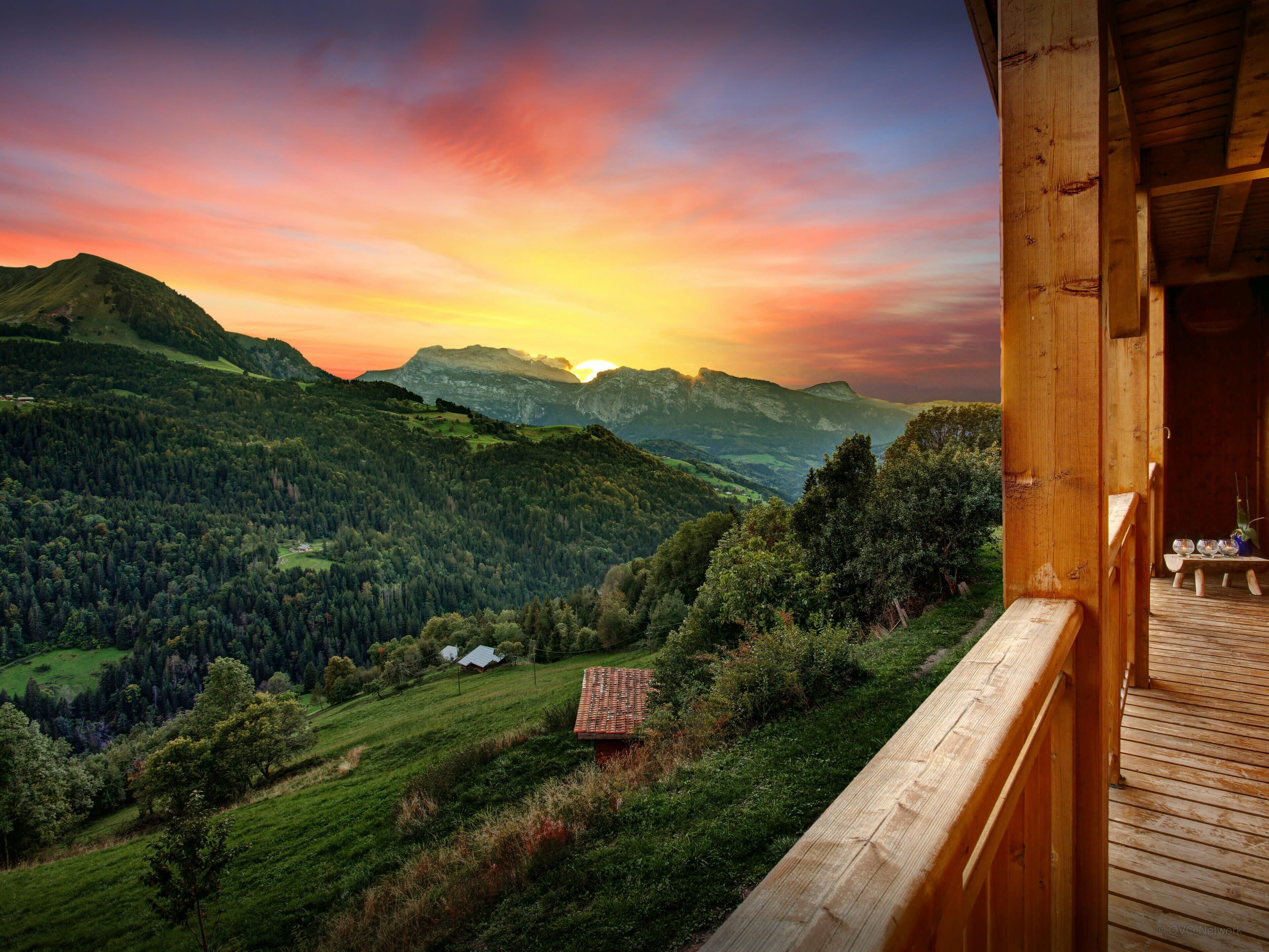 A wooden deck overlooking a mountainous landscape with a sunset.