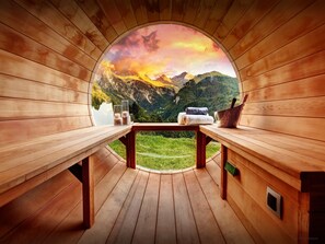 Une cabane en bois dotée d’une lucarne circulaire offrant une vue sur les montagnes. À l’intérieur, on trouve des bancs en bois, une table ainsi que des serviettes et des bougies.