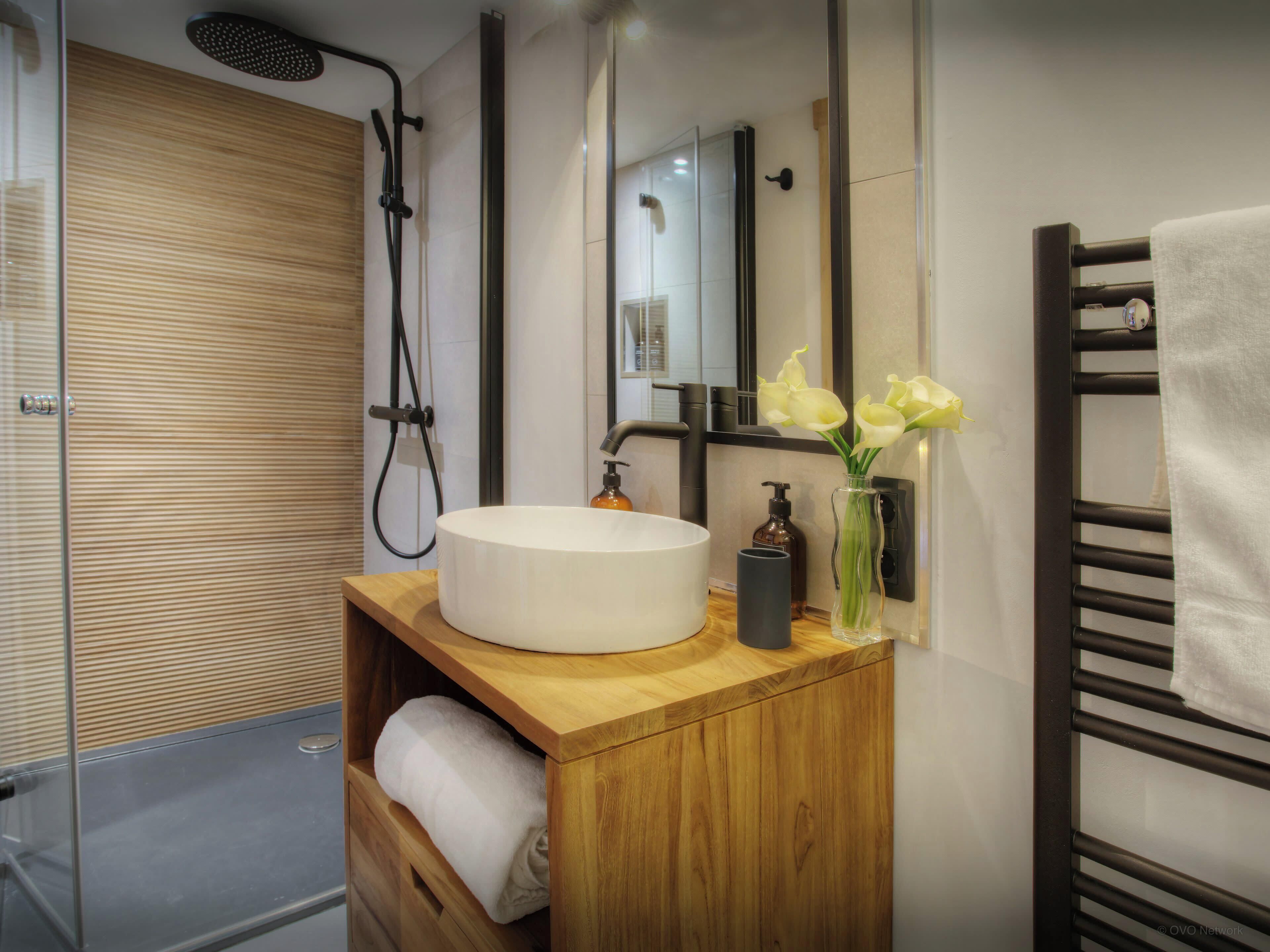 Un baño moderno con un mueble de tocador de madera, un lavabo blanco, un espejo y un perchero para toallas.