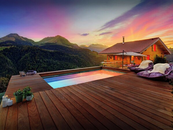 Una terraza de madera con piscina, mobiliario exterior y vista a la montaña.