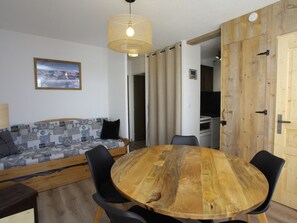 A cozy living area with a wooden dining table surrounded by chairs, a patterned sofa, and a hanging light fixture. - Renovated 5 pers. apartment with south balcony, station center (La Toussuire)