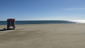 Una playa con un pequeño edificio, cielo despejado y mar tranquilo.