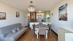Una sala de estar con sofá, una mesa de comedor con sillas, una cocina al fondo y un cuadro en la pared.