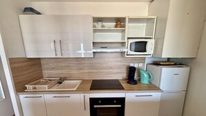 Una cocina compacta con armarios blancos, microondas, cafetera y lavavajillas.