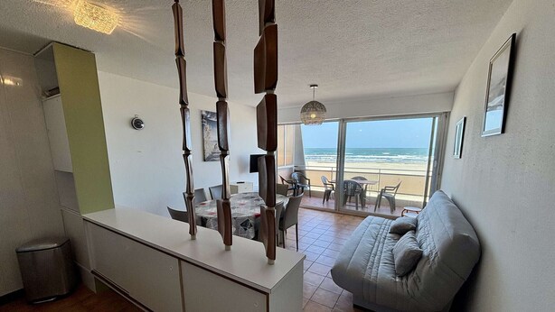 Una sala moderna con sofá, mesa de comedor y sillas, zona de cocina y balcón con vista a la playa.