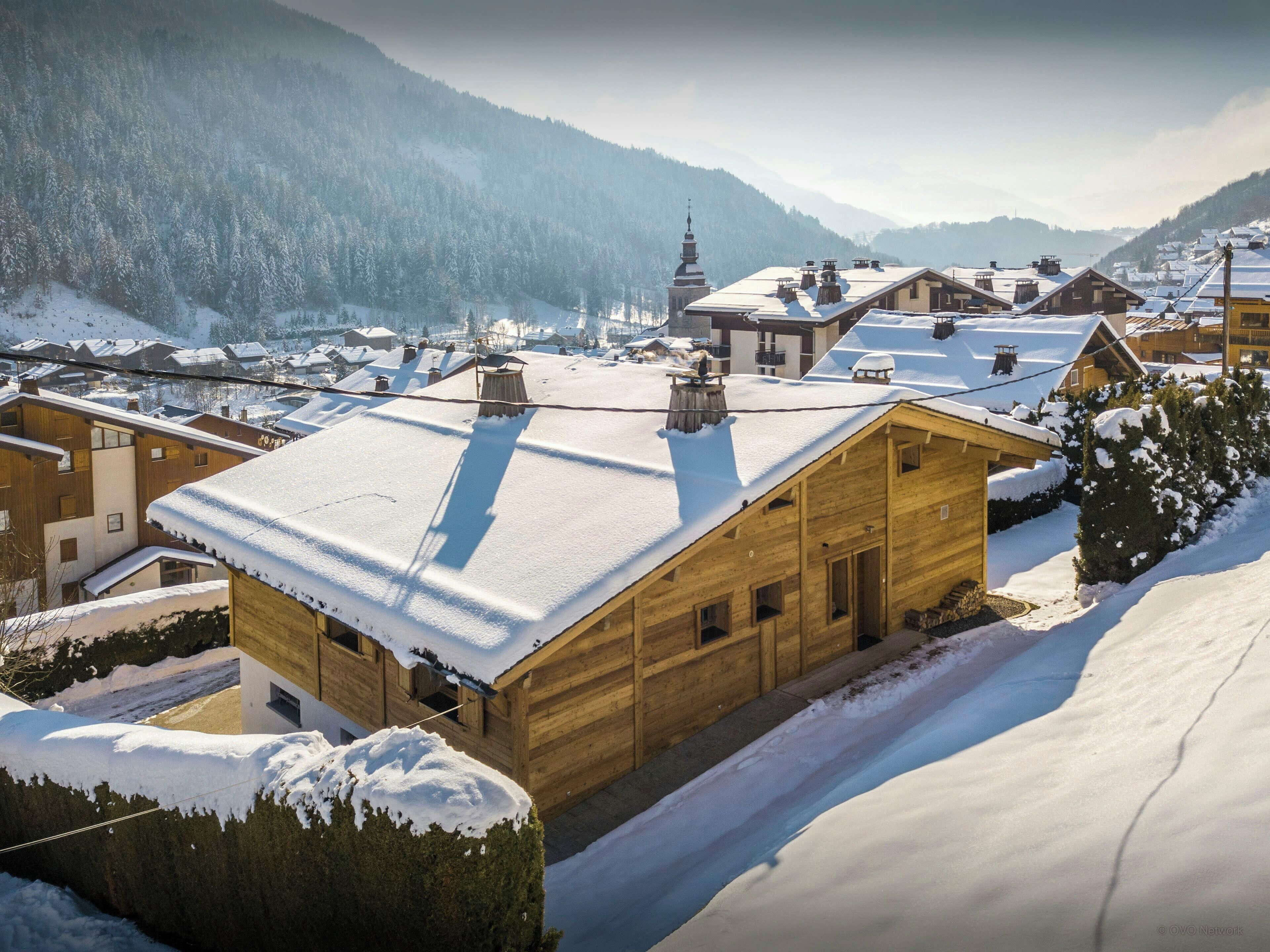 Un chalet en bois, dont le toit est recouvert de neige, niché au cœur d’un paysage montagneux.