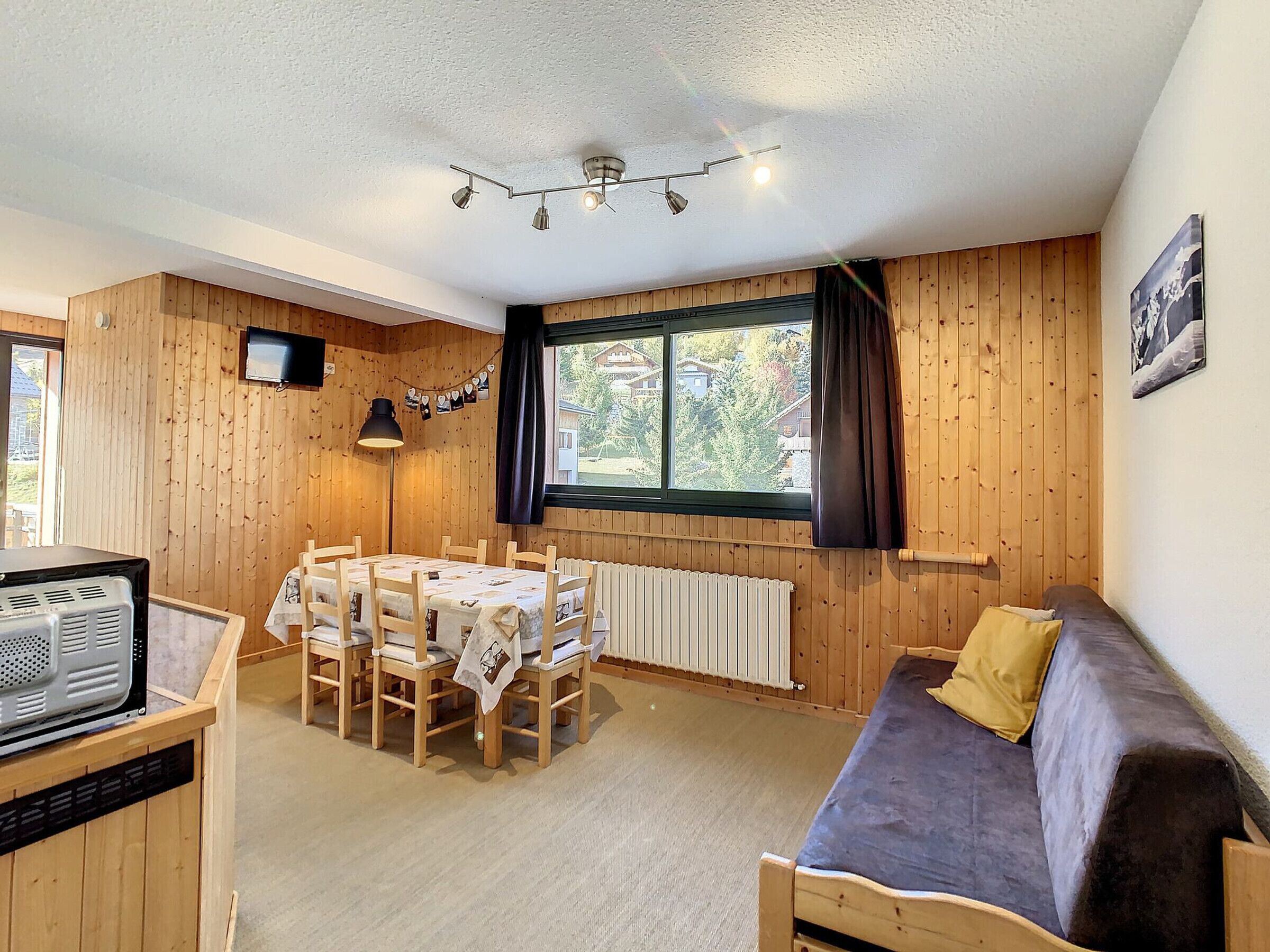 A cozy room with a wooden interior, a dining table with chairs, a sofa, a television, and a window with curtains.