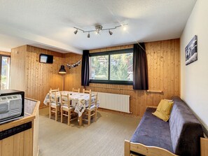 A cozy room with a wooden interior, a dining table with chairs, a sofa, a television, and a window with curtains. - Bright apartment for 6, near slopes, WIFI included (La Toussuire)