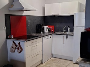 A compact kitchen with white cabinets, a red backsplash, a black coffee maker, and a white refrigerator.