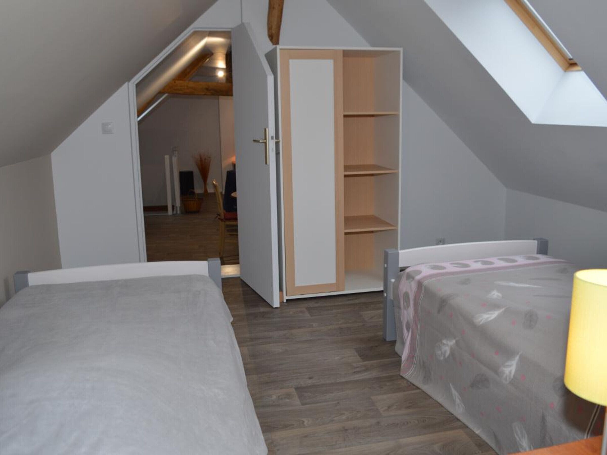 A bedroom with a sloped ceiling, a built-in wardrobe, and a bed with a patterned bedspread.