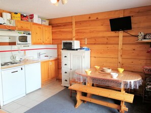 A compact kitchen with wooden cabinets, a microwave, a small refrigerator, and a dining table with a bench. - 2-room apartment for 4 people in Morillon 1100, at the foot of the slopes (Morillon 1100)