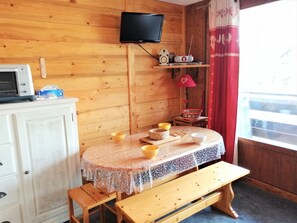 A cozy room with a wooden interior, a television mounted on the wall, a table with a lace tablecloth, and a bench. - 2-room apartment for 4 people in Morillon 1100, at the foot of the slopes (Morillon 1100)