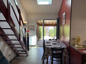 A dining area with a table set for two, a staircase, and a view of the outside. - Sunny Beach Getaway: Cozy 2-Room Mezzanine with Pool, Near Beach, Pet-Friendly (Fleury-Saint-Pierre-la-Mer)