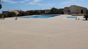 Zona de piscina con cielo despejado, una pileta pequeña y edificios al fondo.