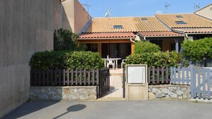 Un edificio residencial con techo de tejas, entrada protegida por una verja y un pequeño espacio al aire libre con mobiliario.
