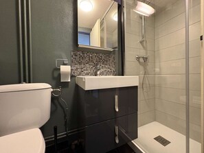 Kylpyhuone, jossa on wc, peilillä varustettu pesuallas, suihku ja laatoitettu seinä.