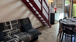 Una sala de estar con un sofá, una mesa de comedor con sillas, una escalera y una lámpara.