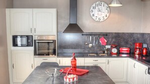 Une cuisine moderne avec des meubles blancs, un îlot central, un four à micro-ondes, un four et une horloge murale.