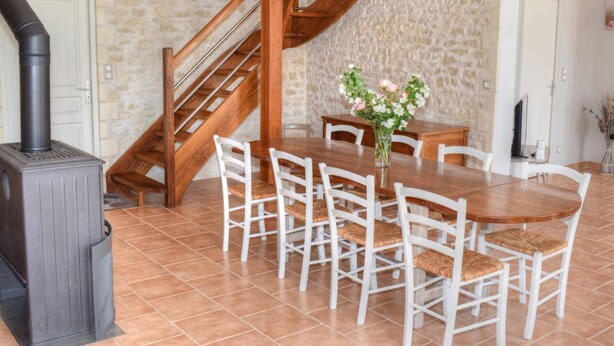 Un coin repas avec une table et des chaises en bois, un mur en pierre et un escalier.