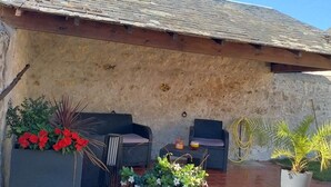 Un patio couvert aménagé avec du mobilier d’extérieur, des plantes en pot et un mur en pierre.