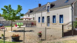 Un bâtiment à deux étages avec une cour en gravier, un vélo et des plantes en pot.