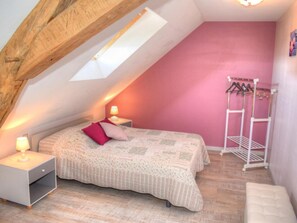 A bedroom with a sloped ceiling, a bed with a pink pillow, a bedside table with a lamp, and a clothing rack.