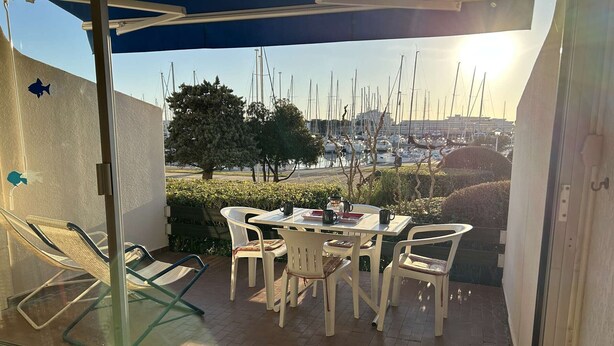 Une terrasse avec une table et des chaises, donnant sur une marina où sont amarrés des bateaux.