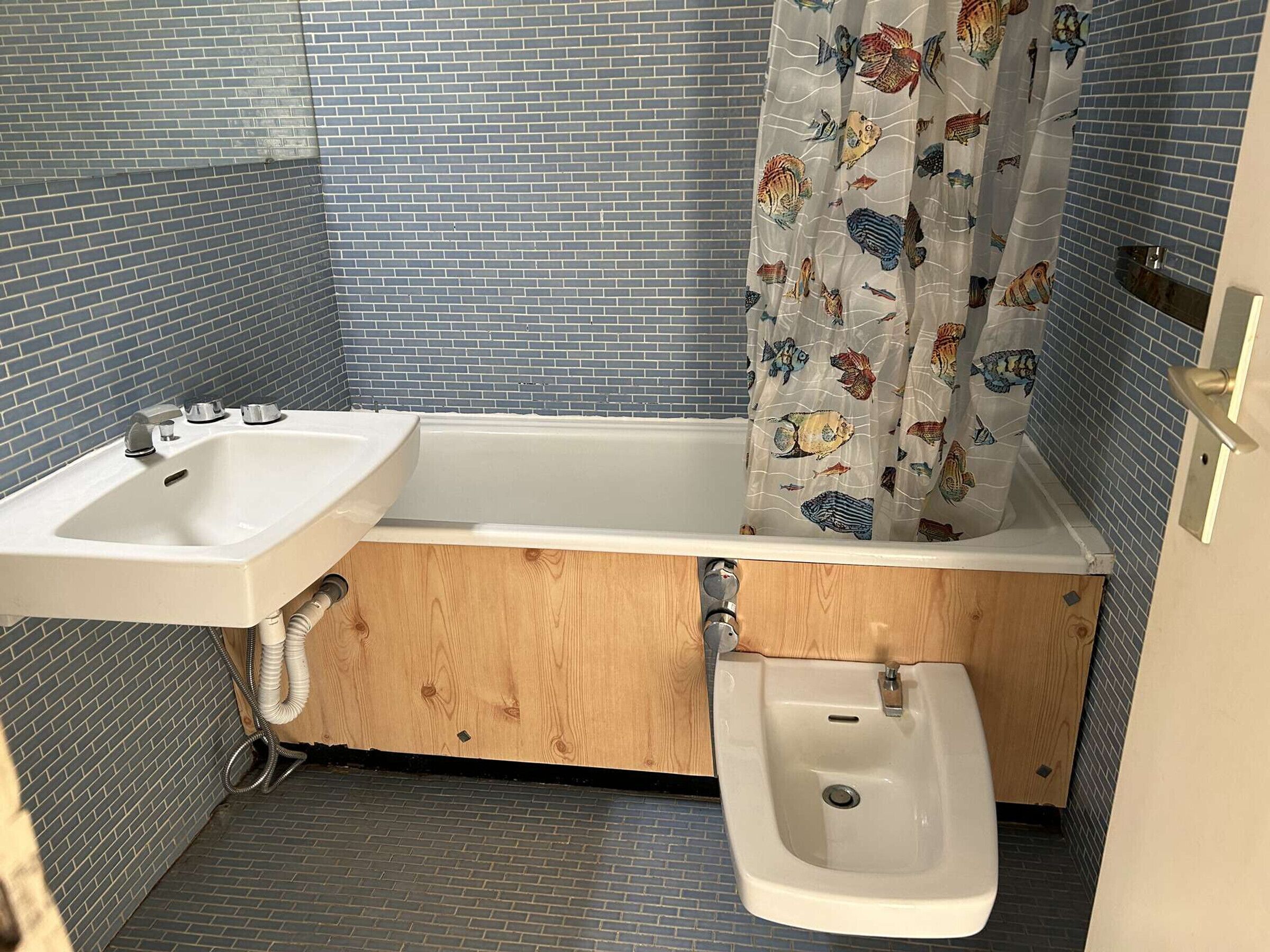 Un baño con lavamanos, bañera y bidé. Las paredes están revestidas con diseños azules y grises.