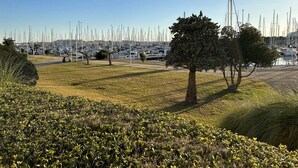 Un port de plaisance où sont amarrés de nombreux voiliers, une zone herbeuse avec des arbres et un ciel dégagé.