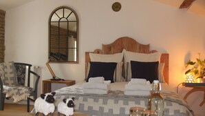 Ein ordentlich eingerichtetes Schlafzimmer mit einem großen Bett, einem Holz-Kopfteil, einem Spiegel, einem Nachttisch mit Lampe und einem kleinen Tisch mit dekorativen Gegenständen.