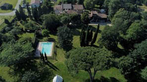 Vue aérienne d’un quartier résidentiel avec une piscine entourée d’arbres et une grande maison dotée d’un toit en tuiles.
