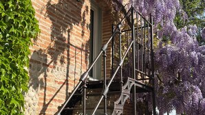 Ein Backsteinhaus mit schmiedeeiserner Treppe und lila blühenden Weinreben.