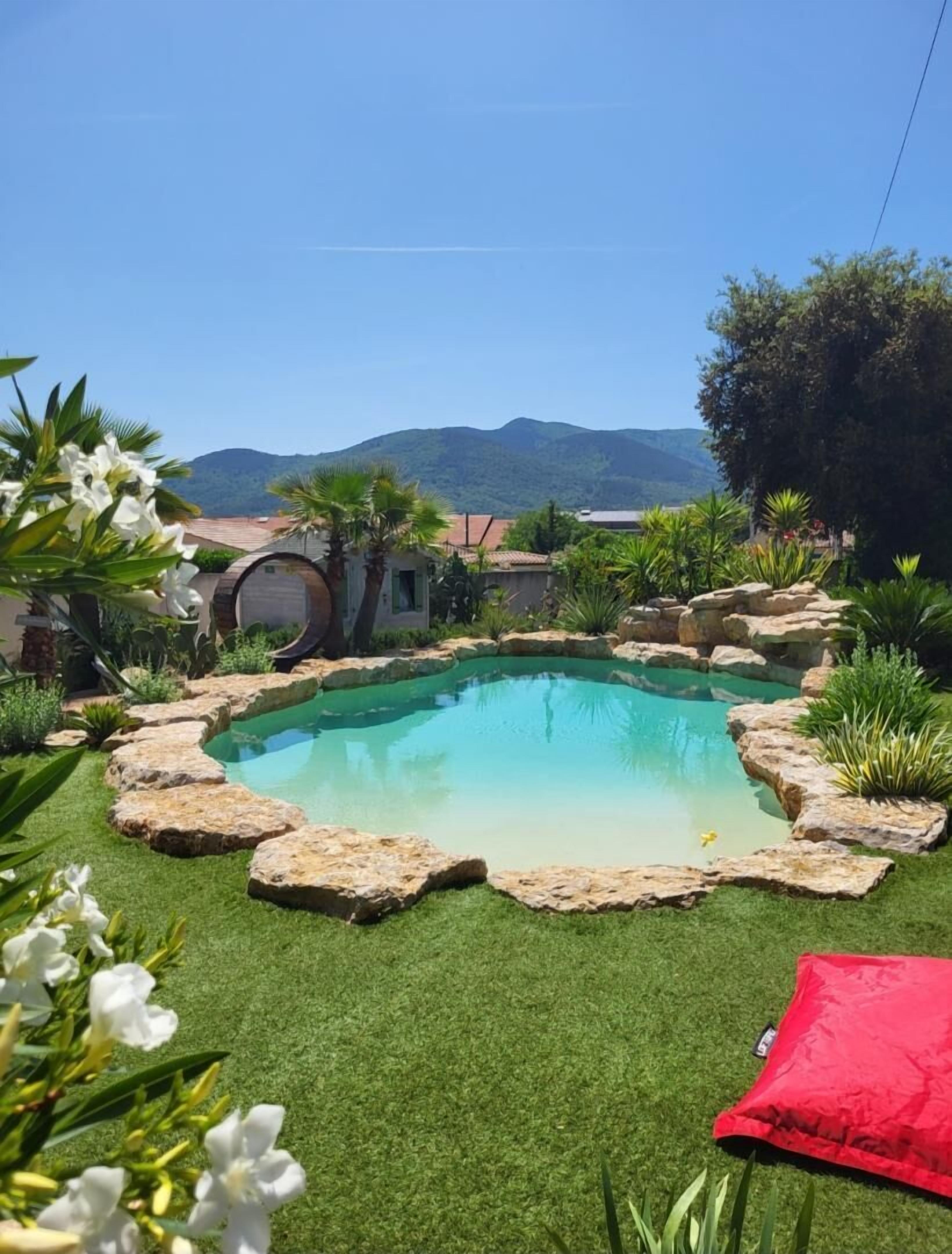 Una piscina envoltada de roques i vegetació, amb una muntanya al fons.