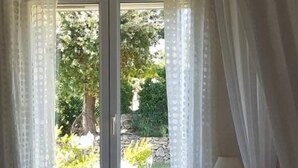 Un dormitorio con cama, cortinas y vistas al exterior con vegetación.
