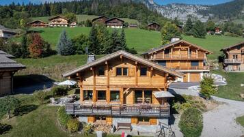 A wooden chalet with a balcony, surrounded by a lush green landscape and mountains in the background.