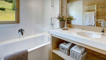 Une salle de bain moderne avec une baignoire, un lavabo et un grand miroir. On trouve des paniers en osier sous le lavabo et une serviette accrochée au mur.