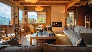 A cozy wooden cabin interior with a fireplace, comfortable seating, and large windows offering a scenic view.