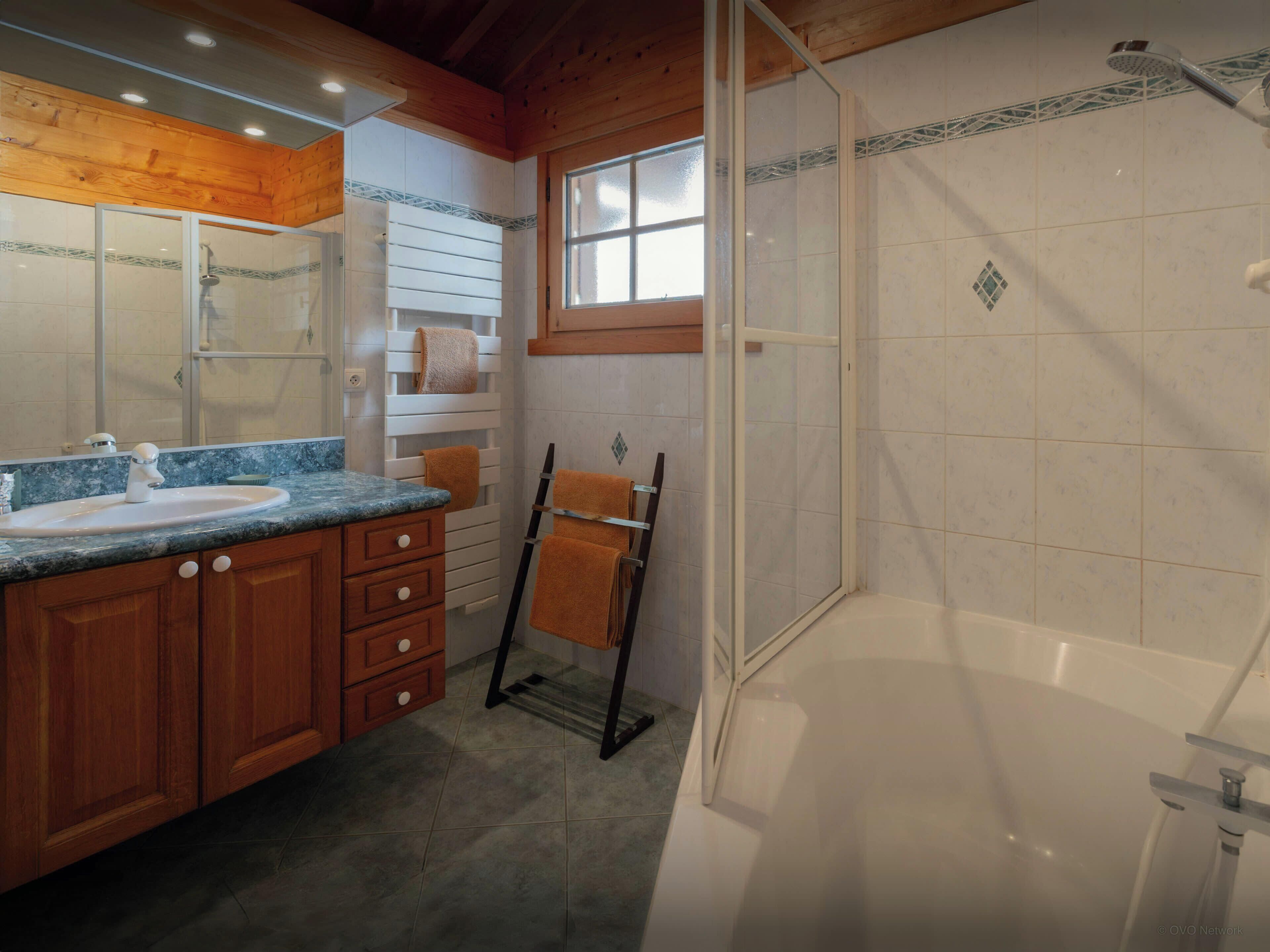 Un baño con ducha, lavamanos y tocador con cajones.