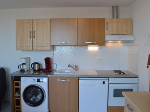 A compact kitchen with wooden cabinets, a washing machine, a dishwasher, a coffee maker, and an oven.