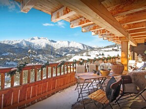 Une terrasse en bois avec une table et des chaises, offrant une vue sur un paysage montagneux enneigé.