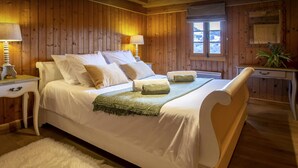 Een kamer met houten lambrisering, een bed, twee nachtkastjes, een venster en een spiegel.