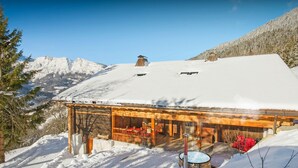 Een houten chalet met een met sneeuw bedekte dak, een jacuzzi en uitzicht op besneeuwde bergen.