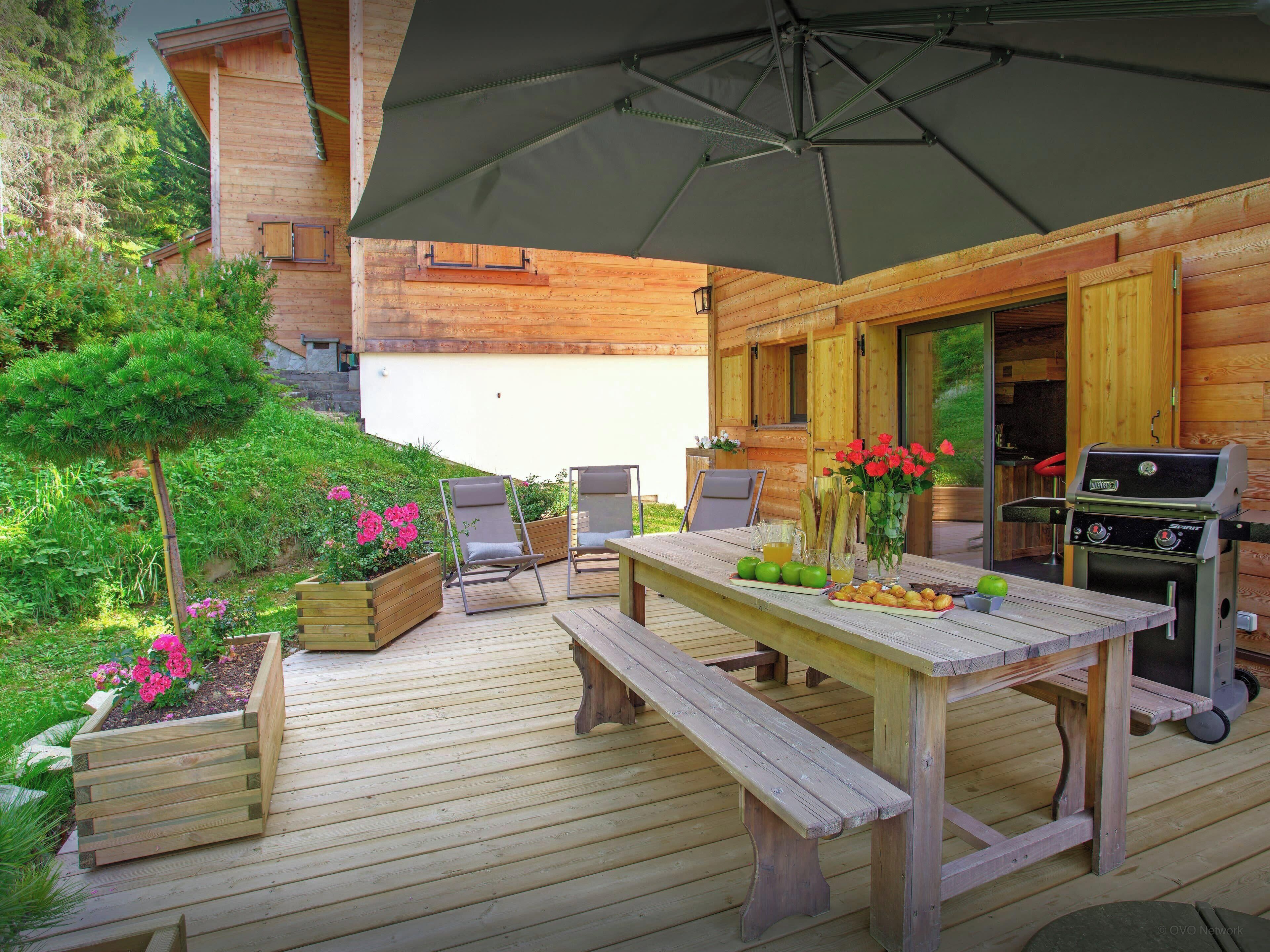 Eine Terrasse im Freien mit Holzmöbeln, einem Grill und einem Tisch mit Speisen und Getränken.