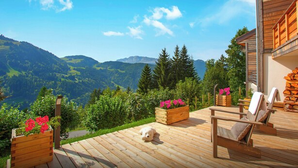 A wooden deck with a scenic mountain view, wooden chairs, and flower planters. - Chalet Charmar - secluded ski-in ski-out chalet for 12 - OVO Network (La Clusaz)