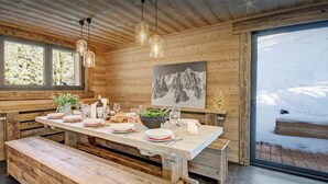 A wooden interior with a dining table set for four, benches, and a view of snow outside. - Chalet Charmar - secluded ski-in ski-out chalet for 12 - OVO Network (La Clusaz)